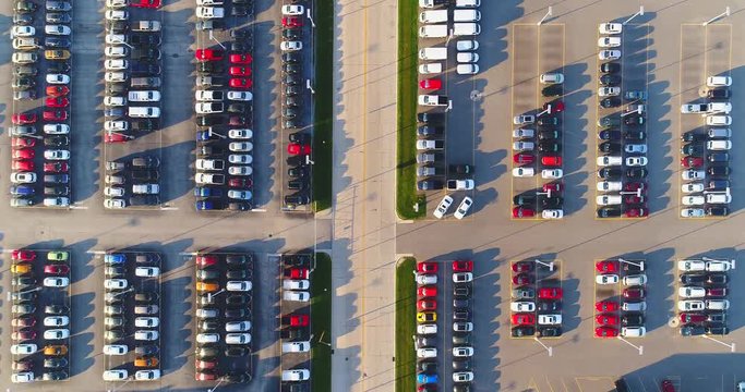 Looking straight down on new car lot, many vehicles for sale, aerial view.
