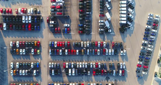 Looking straight down on new car lot, many vehicles for sale, aerial view.
