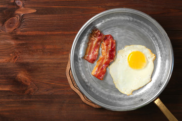 Delicious over easy egg with bacon in pan on wooden background