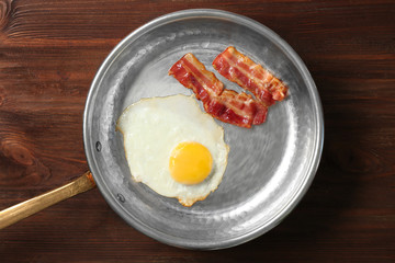 Delicious over easy egg with bacon in pan on wooden background