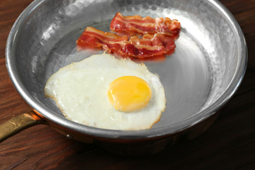 Delicious over easy egg with bacon in pan, closeup