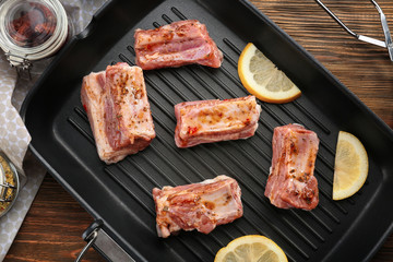 Grill pan with raw pork ribs and lemon slices on wooden table, closeup