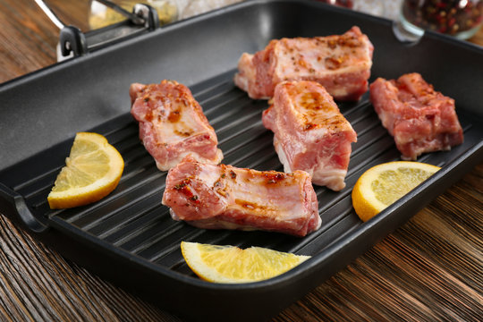Grill pan with raw pork ribs and lemon slices on wooden table, closeup