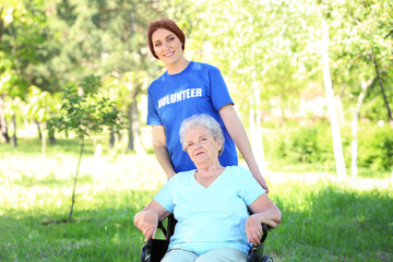 Happy senior woman on wheelchair with young female volunteer outdoors