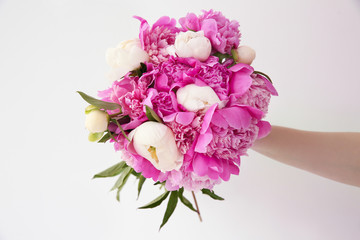 Female hand holding beautiful bouquet with fragrant peonies on light background