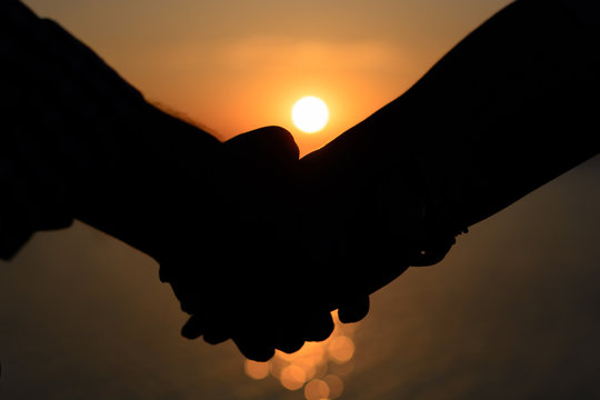 A loving couple (silhouettes of a man and a girl) hold hands in the rays of light at sunset on the sea on a pier.