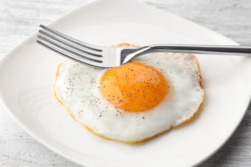 Plate with sunny side up fried egg on wooden table