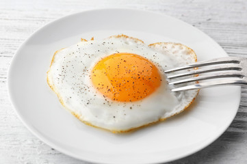 Plate with sunny side up fried egg on wooden table
