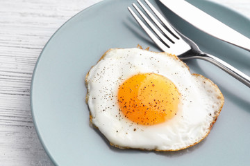 Plate with sunny side up fried egg on wooden table