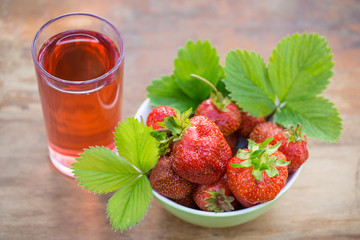 Strawberries in a bowl and a glass of strawberry juice on a wooden table