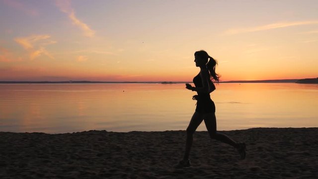 Young athlete runner is runing along the shore of the lake at sunset