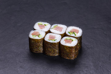 Traditional delicious Japanese food, sushi roll with pink salmon and cucumber served on black slate.