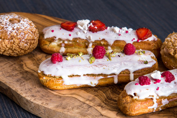 Delicious eclairs with berries and tasty shu cakes on a wooden olive board 