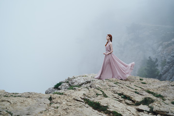 Young beautiful woman in a long dress at the edge of a mountain cliff