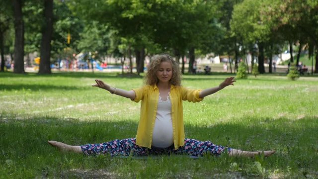Portrait of young beautiful pregnant caucasian woman, girl doing yoga exercise in park, sitting on grass, lotus position. Pregnancy, motherhood.Hd