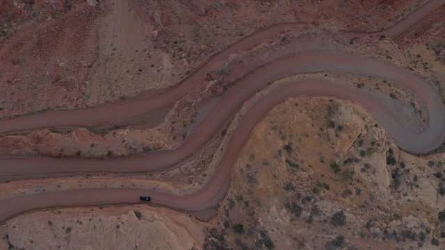 AERIAL TOP DOWN: Black SUV car driving up a winding switchback road on mesa mountain cliff in red rock desert. 4x4 jeep vehicle traveling on dangerous hairpin Moki Dugway carved into the cliff edge