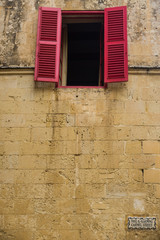 Fototapeta na wymiar Limestone building with open window and red shutters, Mdina, Valletta, Malta
