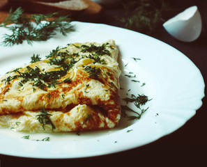 Tasty omelette with greens on a white plate, bread and chicken eggs on a dark wooden background