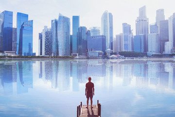 man standing on the pier looking at modern cityscape skyline with reflection in water