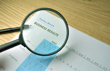 Business report on a wood tabletop with a pen and a magnifying glass
