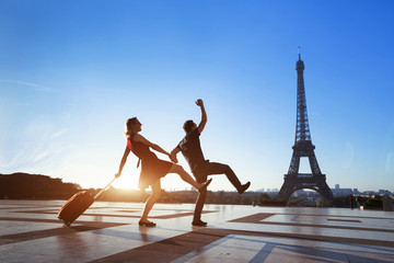 Naklejka premium para szalonych turystów na wakacjach w Paryżu, mężczyzna i kobieta bawią się blisko Wieży Eiffla, podróżują z bagażem, turystyka