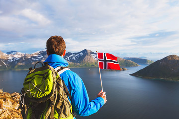travel to Norway, hiker traveler with backpack holding norwegian flag and looking at beautiful...