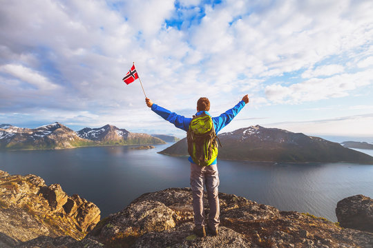 travel to Norway, happy tourist hiker with backpack standing on the top of mountain and holding norwegian flag