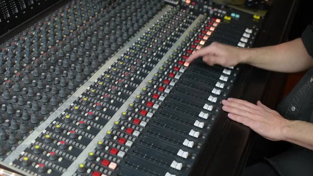 Hands moving faders on audio mixing desk 