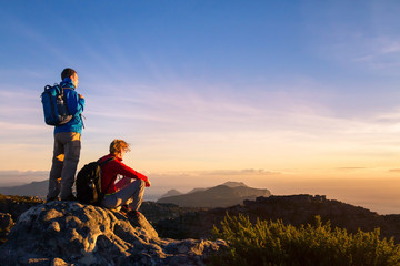 couple of hikers with backpacks enjoying panoramic view of sunset in mountains, travel and outdoor...
