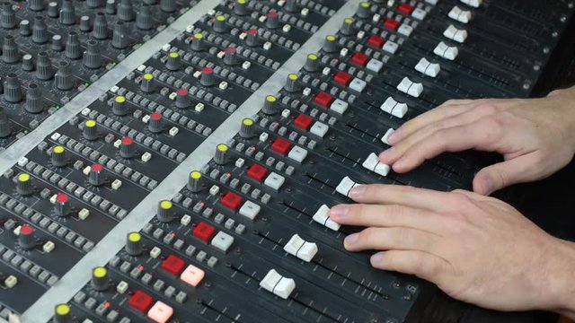 Hands moving faders on audio mixing desk 
