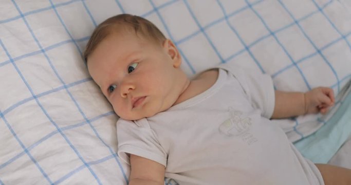 adorable baby boy lying pillow white watching cute infant toddler looking around emotion moving head hands chubby cheeks home child kid two months newborn face side view brown hair quiet calm relaxed