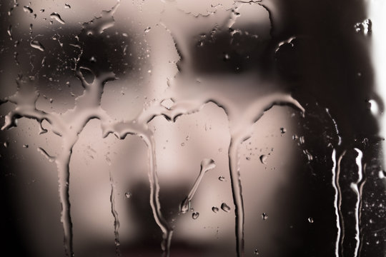 sad female blurred face looking through glass with water drops