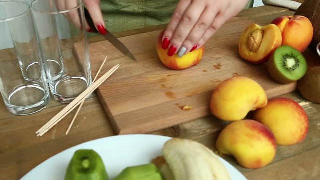 Preparation for a fruit cocktail on a cutting board of bananas, strawberries, peaches. Woman regiment knife peach Moving camera left to right