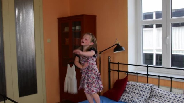 Cute little girl dances and jumps on a bed. Small girl wears flowered dress. Childhood concept