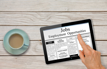 Online job hunting Hand with computer tablet reading employment ads on table with coffee

