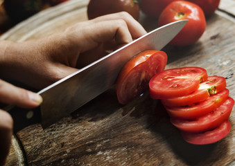 Hands holding a knife slicing a tomato