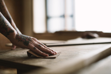 Hands with tattoo using sandpaper on a wood