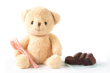 Bear doll sitting with chocolate brownie cake with pink spoon white background isolated.