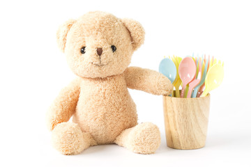 Bear doll sitting with colorful plastic spoon in wooden glass isolated.