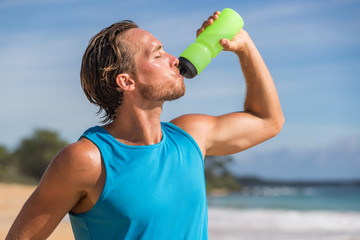Sports bottle drink sport man drinking water on beach run. Male runner sweaty and thirsty after difficult workout.