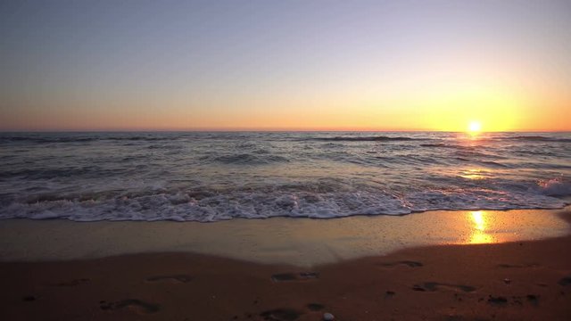 Romantic sunset background video without people - gentle waves slowly washing out a couples footsteps in the sand