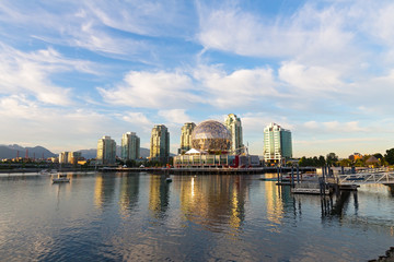 Golden sunset at False Creek in Vancouver with a view on Science World and mountains. Urban sunset with landmark reflection in the water.