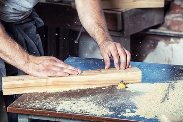 Close-up as a young man gray t-shirt by profession carpenter builder equals a wooden milling machine on a wooden table in the workshop