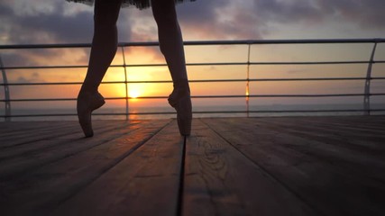 Close up of a ballet dancer's feet as she practices pointe exercises on the embankment near sea or ocean, sunrise background, Silhouette of woman's feet in pointe shoes. Ballerina shows classic ballet