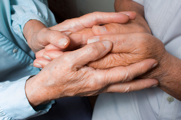 Hands of two loving senior people on a dark background