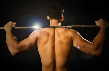 Back view of fitness and bodybuilder man lifting the barbell, showing his back, shoulders, triceps, biceps muscles on black color background and rim light