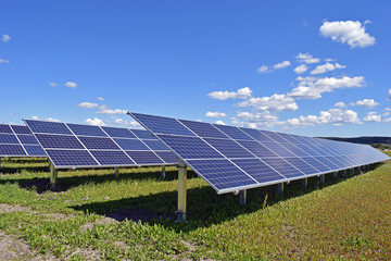 Solar panels on field. Clear blue sky with a few small clouds on background. Horizontal image with space for text.