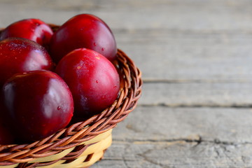 Fresh sweet plums in a wicker basket on a vintage wooden background with copy space for text. Violet plums harvest closeup