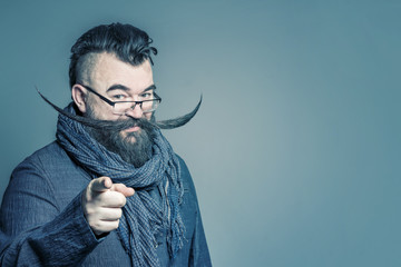 Adult bearded man in a scarf with a long mustache showing the forefinger forward. Toned