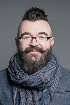 Smiling bearded man in a scarf and glasses with mohawk hairstyle on a gray background
